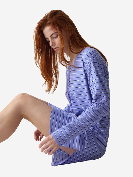 Zittend model met rood haar draagt een lila gestreept nachthemd met V-hals en lange mouwen.