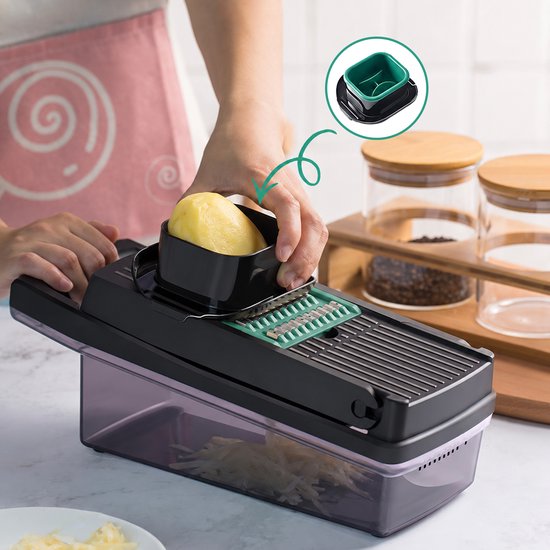Handen die een aardappel door een zwarte groentesnijder met een groen raspblad duwen.
