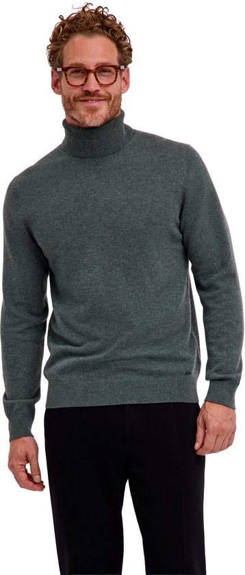 Model met bril in een groene coltrui van kasjmier met een subtiel metalen FALKE-logo aan de onderkant.