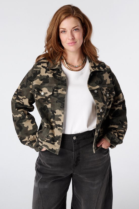 Model in camouflage jas over een wit t-shirt met donkergrijze jeans met wijde pijpen.