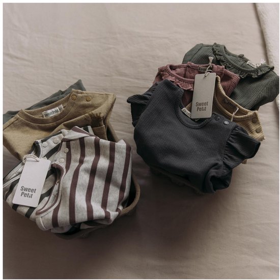 Stapel babykleding in verschillende kleuren met Sweet Petit labels, inclusief gestreepte en effen shirts.