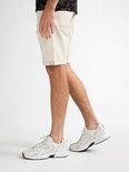Een man met een wit T-shirt en beige spijkerbroek draagt witte sneakers met zilveren accenten en een zwarte zool.