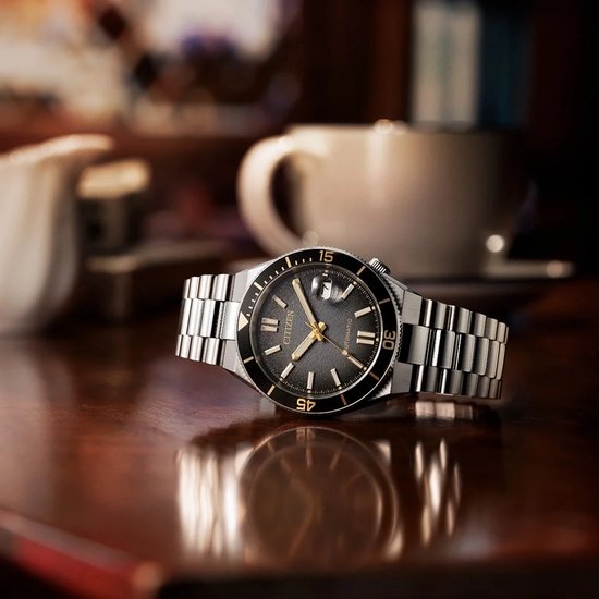 Zilveren horloge met zwarte wijzerplaat en gouden indices, liggend op een houten tafel.