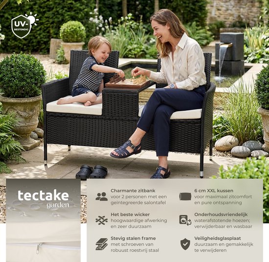 Een vrouw en een jongen spelen schaak op een zwarte polyrattan tuinbank met tafel en beige kussens.