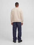 Zijaanzicht van de achterkant van een man in een crème kleurige sweater en donkerblauwe jeans. De sweater heeft lange mouwen en een label op de mouw.