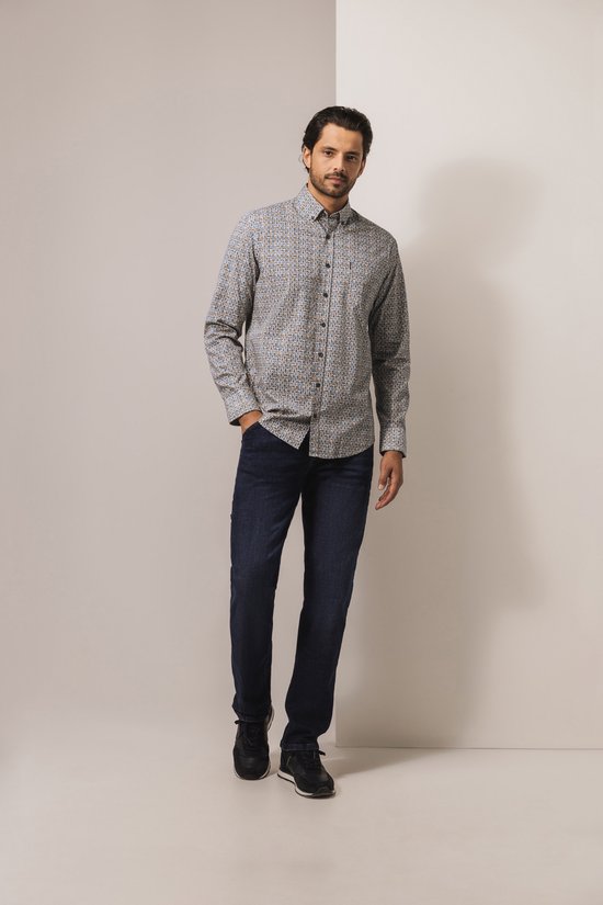 Full-body shot van een model in een State of Art overhemd met bladprint, donkere jeans en casual sneakers.