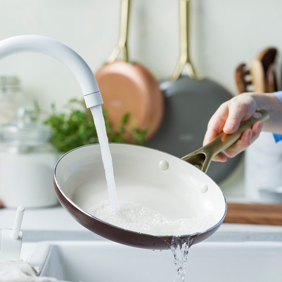 Bruine koekenpan met crème binnenkant wordt afgespoeld onder een kraan in een gootsteen.