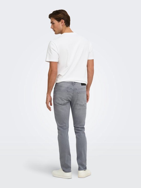 Achterkant van een model in een witte t-shirt en grijze slim fit jeans met witte sneakers.