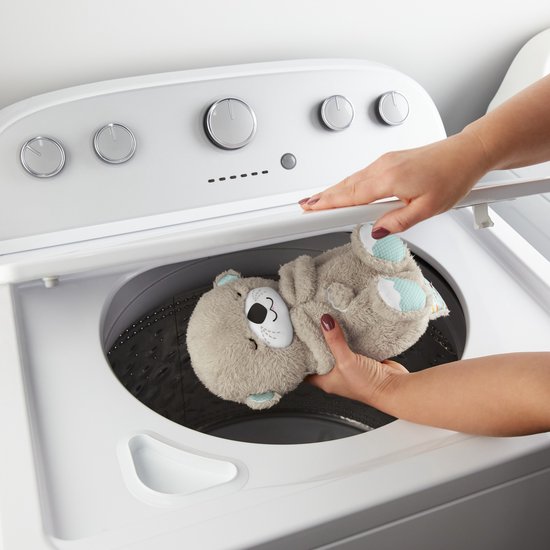 Handen plaatsen een zachte, bruine otter knuffel in een wasmachine.