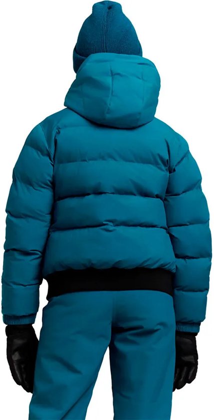 Meisje in donkerblauwe winterjas, skibroek, muts en zwarte handschoenen, gezien vanaf de achterkant.