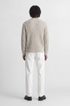 Model in beige grofgebreide trui en witte broek, volledig zicht van achteren.