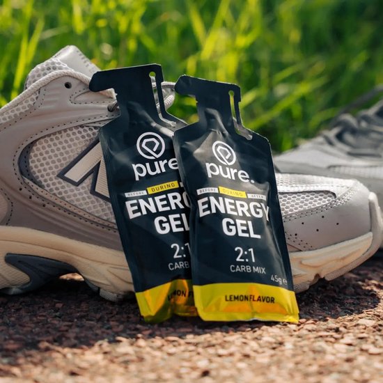 Twee Pure energy gel citroen verpakkingen geplaatst tegen een grijze hardloopschoen op een pad.