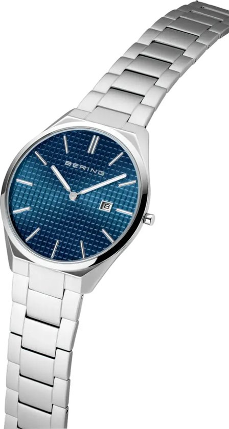 Zilverkleurig horloge met blauwe wijzerplaat met ruitpatroon en datumvenster, schuin van de zijkant gefotografeerd.