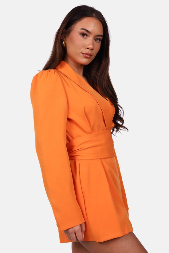 Close-up van het model in een oranje blazerjumpsuit met opvallende schouders en tailleceintuur.