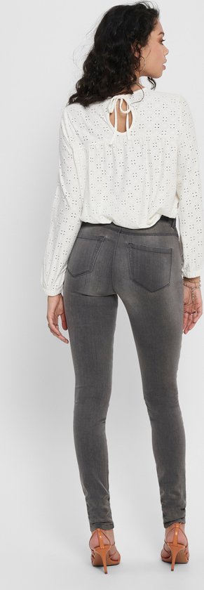 Vrouw van achteren gezien in grijze skinny jeans en een witte kanten blouse.