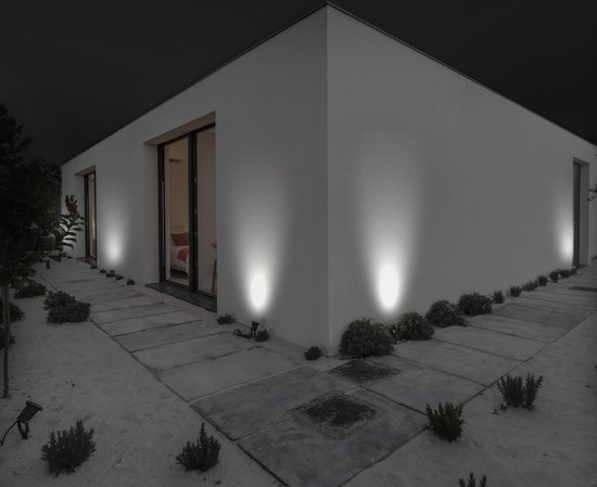 Moderne witte villa 's nachts verlicht door meerdere zwarte LED-spots in de tuin.
