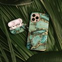 Telefoonhoes en AirPods-hoes met groen en goud marmerpatroon, liggend op groene bladeren.