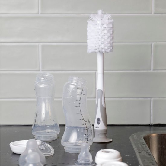 Fles- en spenenborstel met grijze handgreep en grijze zuignap, naast babyflessen op het aanrecht.