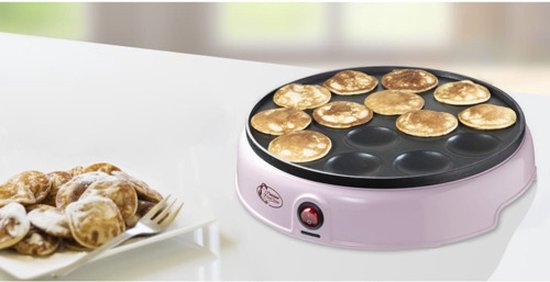 Roze poffertjespan op een tafel, naast een bord met poedersuiker bestrooide poffertjes.
