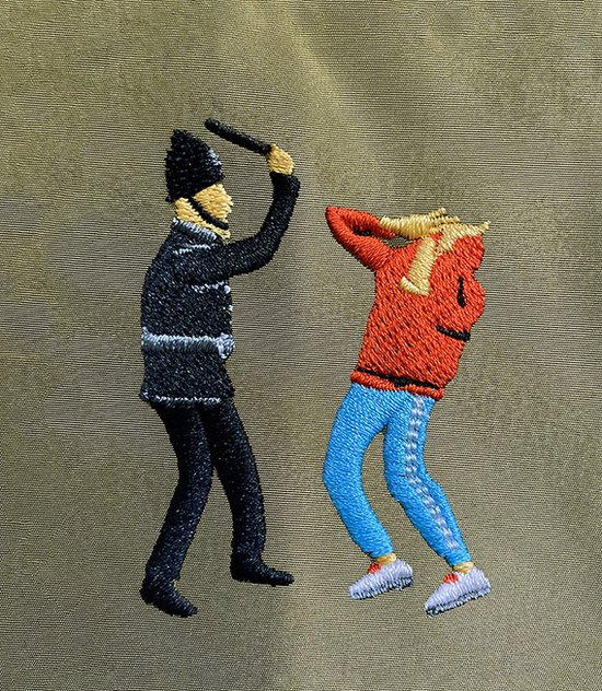 Detail van olijfgroene stof met geborduurde politieagent die een man in rood shirt slaat.