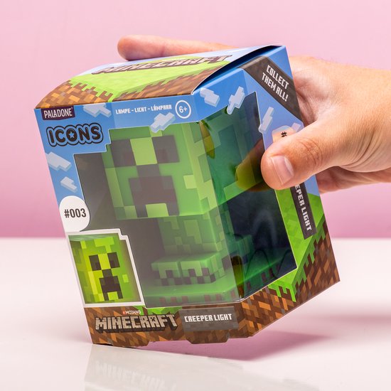 Een hand die de verpakking van de Minecraft Creeper Icon Light vasthoudt, met de lamp zichtbaar binnenin.