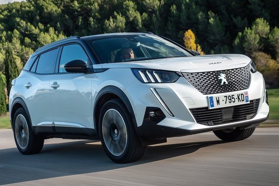 Witte Peugeot 2008 SUV in beweging op een weg, met bomen op de achtergrond.