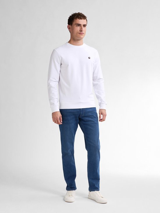 Model draagt een wit shirt en blauwe tapered fit jeans met witte sneakers.