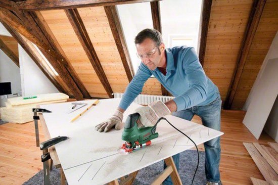 Man met veiligheidsbril en handschoenen zaagt met groene Bosch decoupeerzaag in gipsplaat.