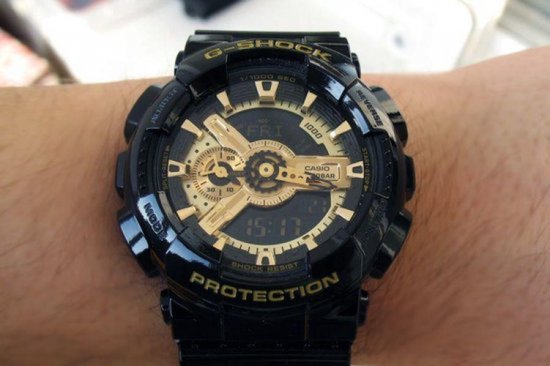 Pols met een zwarte G-Shock horloge met gouden wijzerplaat. Datum en tijd zichtbaar.