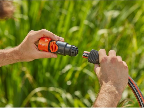 Twee handen verbinden een oranje Gardena Profi System ventiel met een tuinslang.
