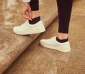 Een persoon die witte sneakers aantrekt met zwarte enkelsokken.