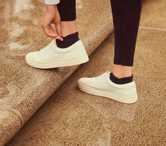 Een persoon die witte sneakers aantrekt met zwarte enkelsokken.