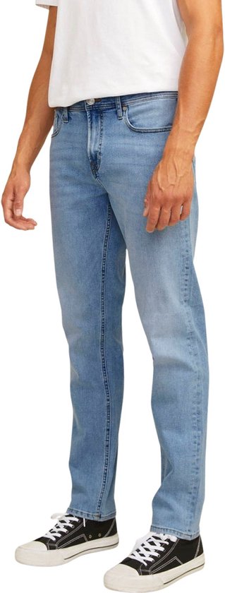 Man met een witte t-shirt en blauwe jeans, staand in profiel. Focus op de jeans.