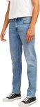 Man met een witte t-shirt en blauwe jeans, staand in profiel. Focus op de jeans.