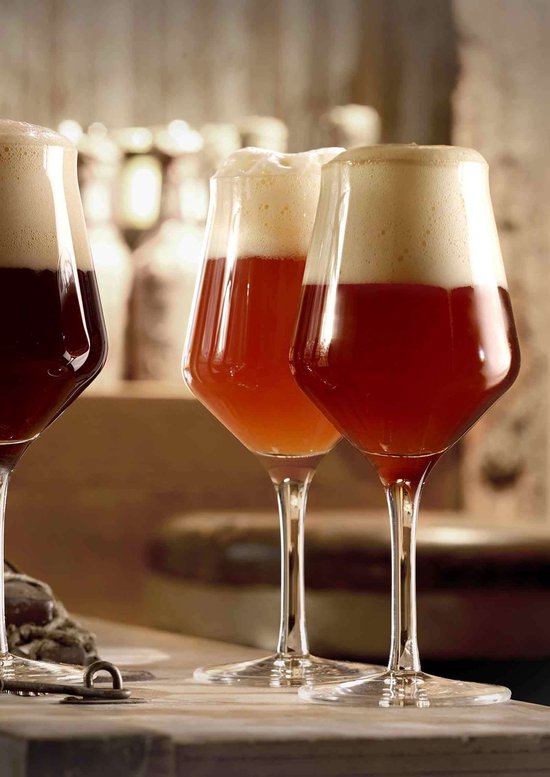 Drie glazen met amberkleurig bier en stevig schuim, met een brede kelk en hoge steel.