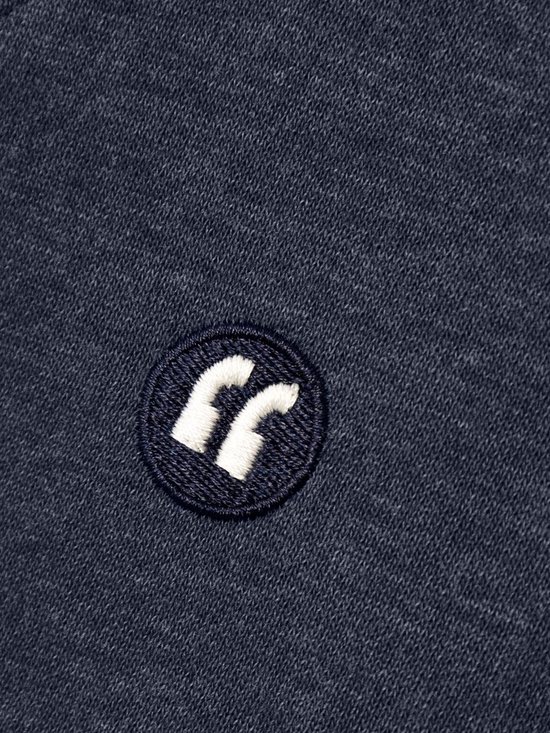 Detail van een geborduurd zwart-wit logo op een donkerblauwe sweater.
