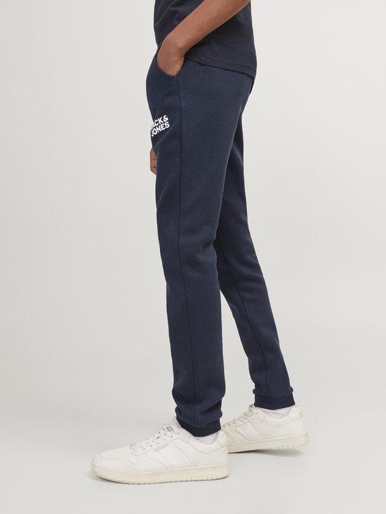 Jongen die een marineblauwe joggingbroek met 'JACK & JONES' opdruk draagt, met witte sneakers.