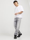 Man met witte T-shirt en grijze jeans, kijkend naar de vloer.
