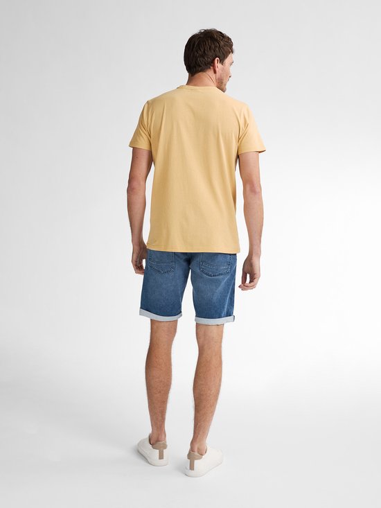 Achterkant van een man met donkergeel T-shirt, blauwe spijkerbroek en witte sneakers.