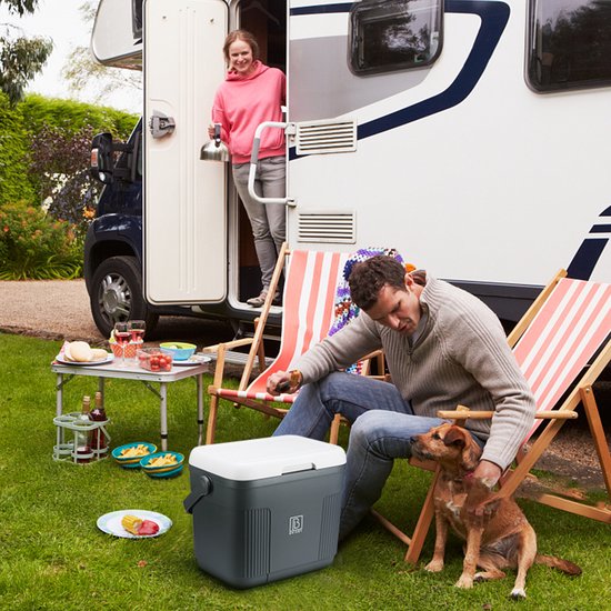Man en hond rusten op ligstoelen naast een grijze Brisby koelbox bij een camper.