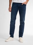 Een man die in een donkerblauwe, slimfit jeans met een witte T-shirt en crèmekleurige sneakers staat.