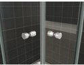 Gros plan sur deux poignées de porte de douche rondes, de couleur argent, avec une finition métallique brossée, placées sur des portes vitrées sur fond de carreaux noirs.