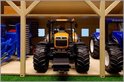 Houten landbouwloods voor 3 tractoren met een gele tractor in het midden en twee blauwe tractoren ernaast.