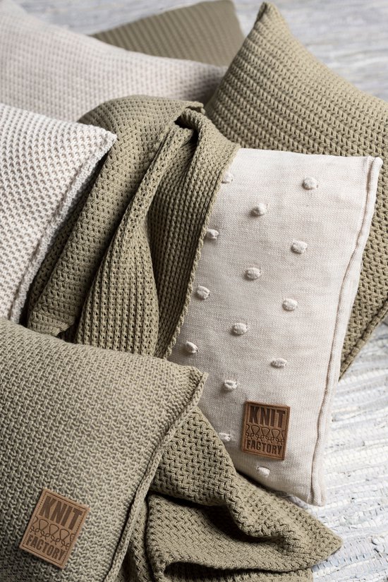 Linnen sierkussen met off-white stof, gedecoreerd met kleine pomponnetjes en een bruin 'Knit Factory' label.