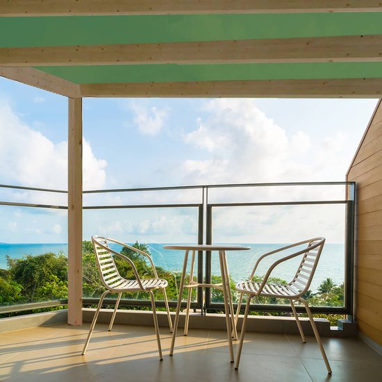 Een balkon met uitzicht op de oceaan. Een ronde tafel met twee witte stoelen staat op het balkon.