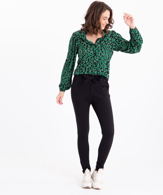 Model met zwarte broek met strikceintuur en groen hartjesblouse.