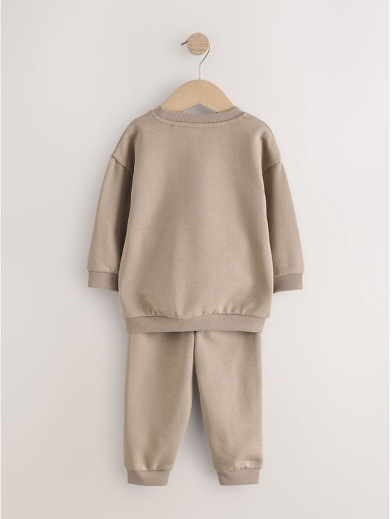 Set van naturelkleurige sweater en joggingbroek met geribbelde boorden, hangend aan een kledinghanger.