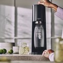Hand die de zwarte SodaStream Terra bedient, naast een glas met limoen en munt.
