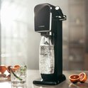 Zwart SodaStream ART bruiswatertoestel met een fles bruiswater, naast een glas en sinaasappelpartjes.