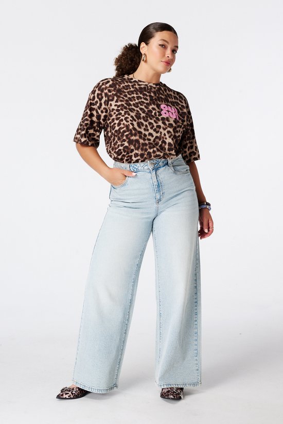 Model draagt een bruin t-shirt met dierenprint en roze 'OUI OUI' borduursel, met lichtblauwe wijde jeans.